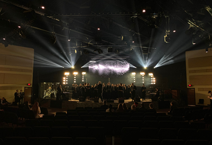 Stage with choir and musicians performing with white light beams