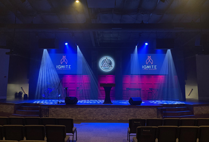 Blue and purple lit stage with white church logo on back wall