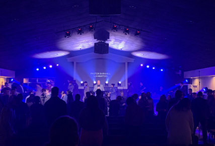 Blue lit room with stage at the front, with the view being obstructed by dark silhouettes of the audience