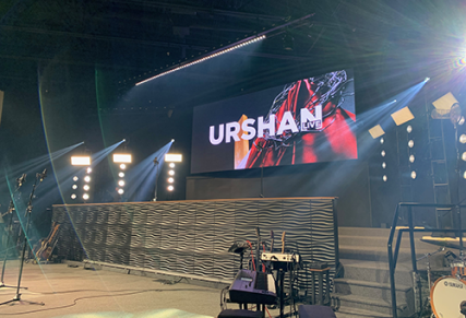 Stage with wall separating front and back stage with screen displaying "Urshan"