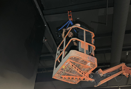 Man standing inside crane lift working on installing lights on interior ceiling